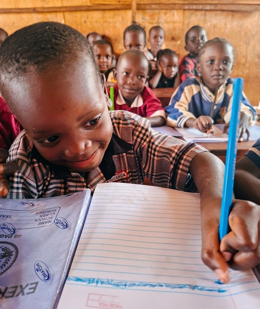A nursery child concentrates on writing in an exercise book with a pencil in a Ugandan classroom