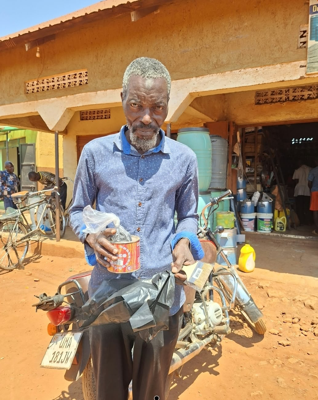 Ndegge holding a tin of varnish and a brush bought by the Foundation to finish his bed frame in Busia