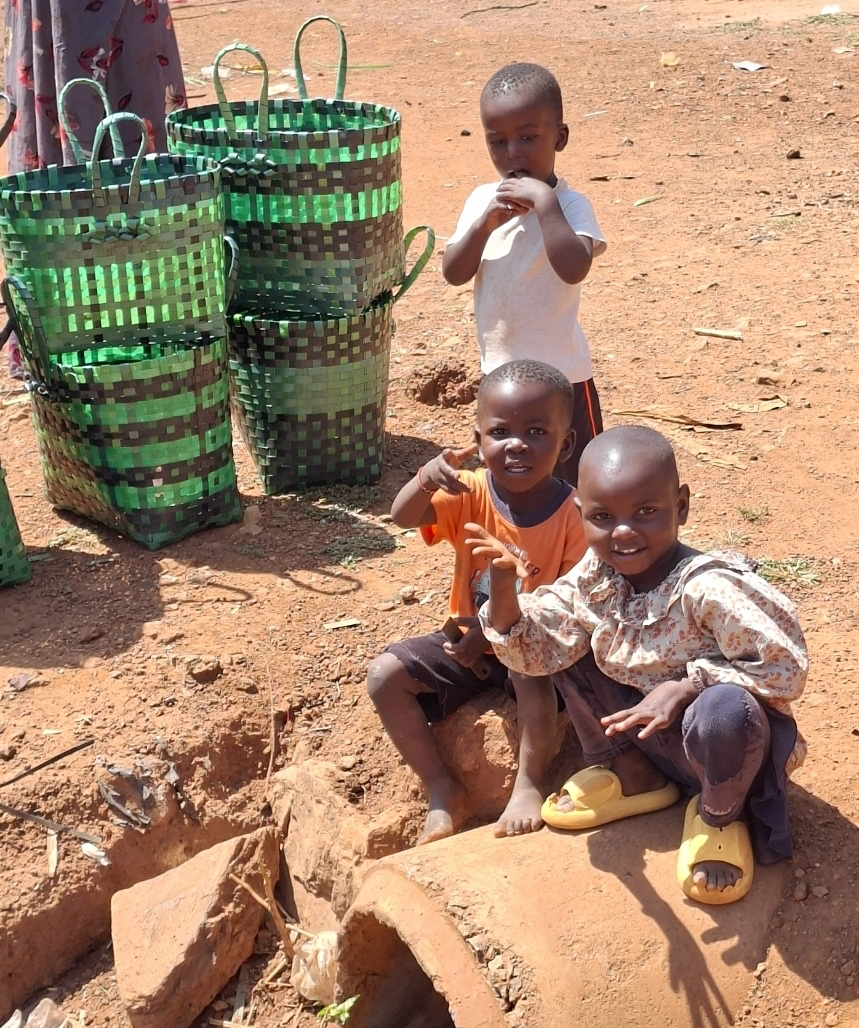 Children sitting beside green woven baskets outside the family home in Mawero, Busia