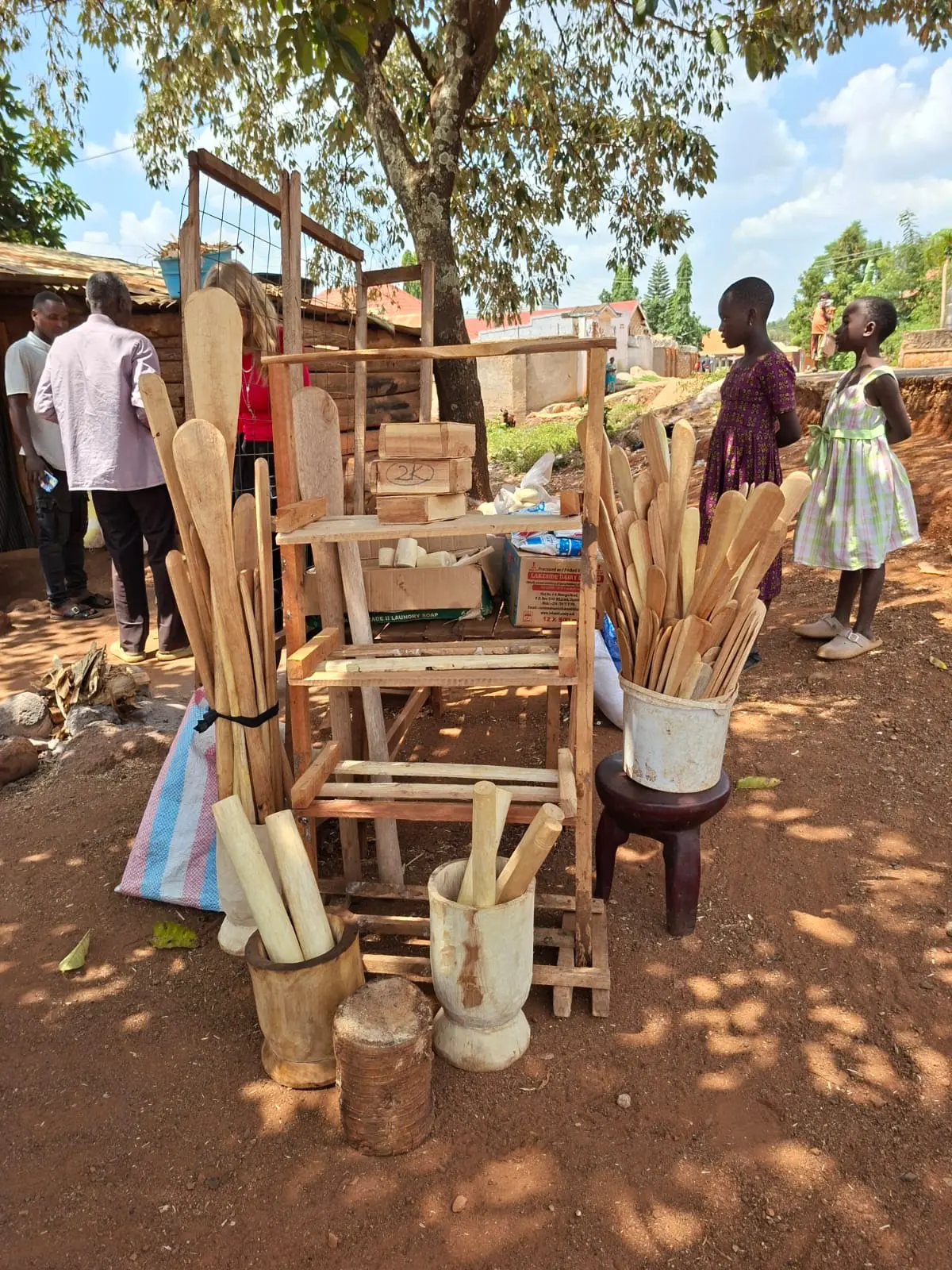 Ndegge's carpentry products and tools displayed under a tree at his outdoor workshop in Mawero, Busia