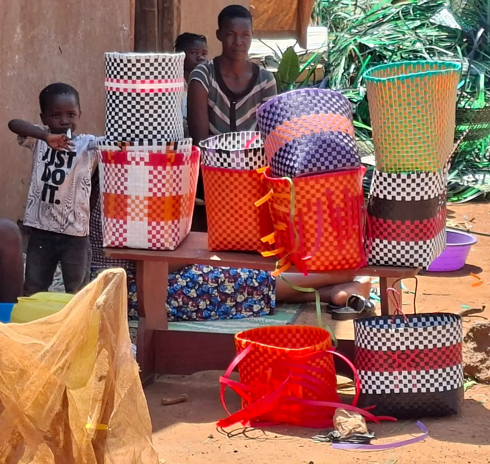 Issa's family beside a display of brightly woven baskets and bags for sale in Mawero, Busia